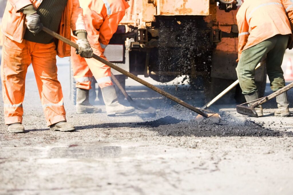 Infrared asphalt repair in progress with crew spreading heated asphalt to restore damaged pavement surface.