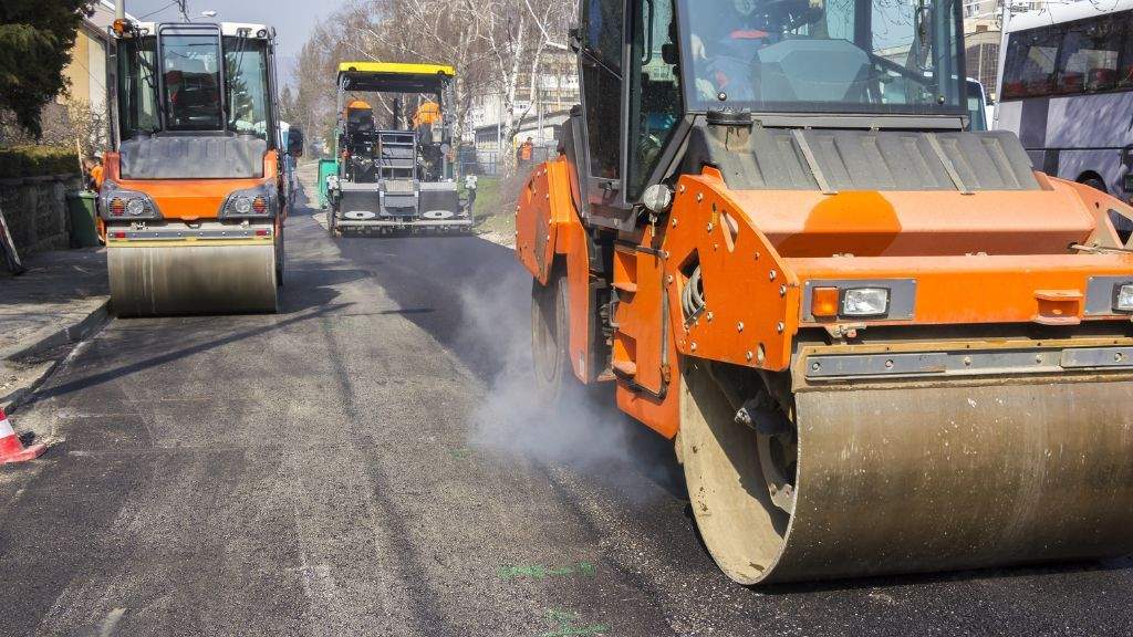 Heavy asphalt rollers compacting freshly laid hot-mix pavement during a fall paving project