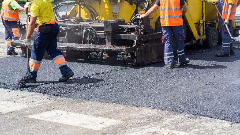 Paving crew members using a lute and finishing tools to level and smooth new asphalt before winter temperatures drop